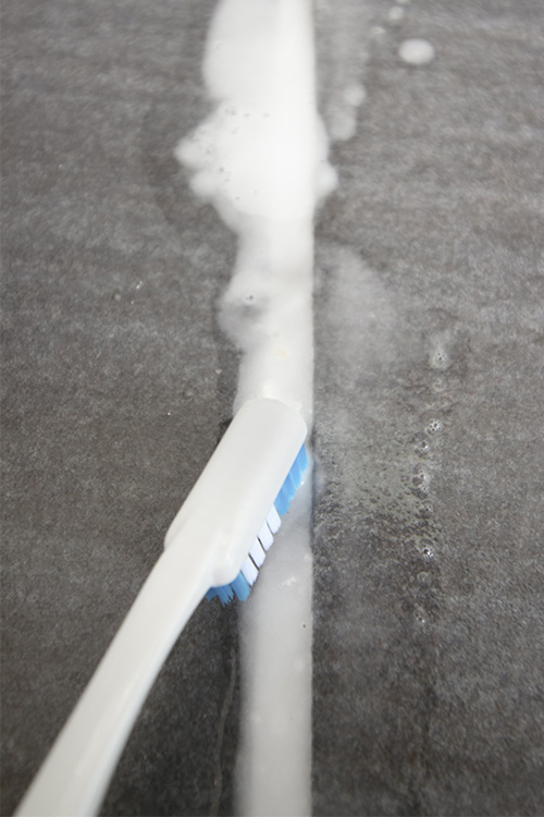 Brushing grout with a toothbrush.