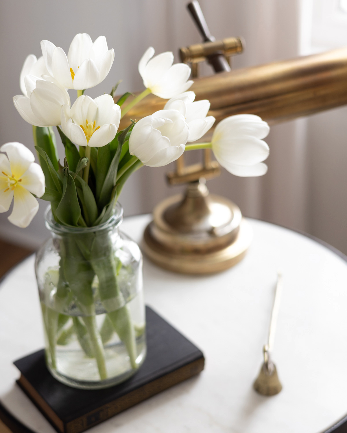 White tulips on a table next to a brass lamp.