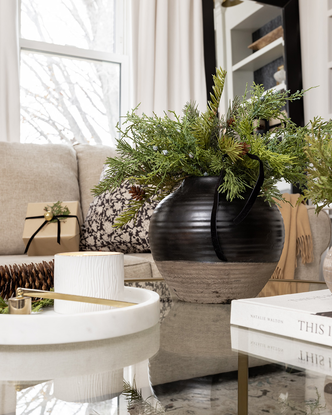 Black vase of Christmas greenery on a glass coffee table.