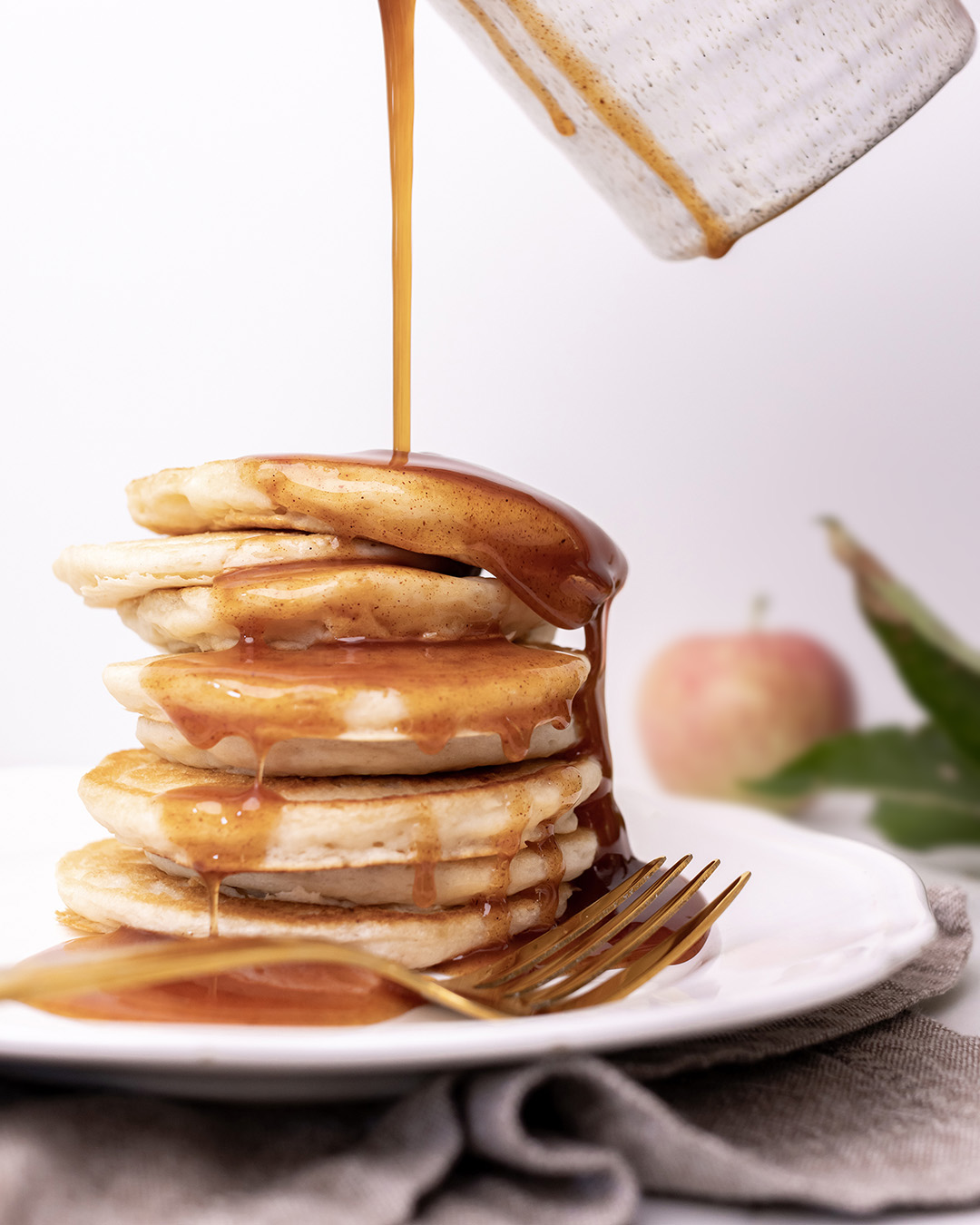 Pouring syrup over a big stack of pancakes.