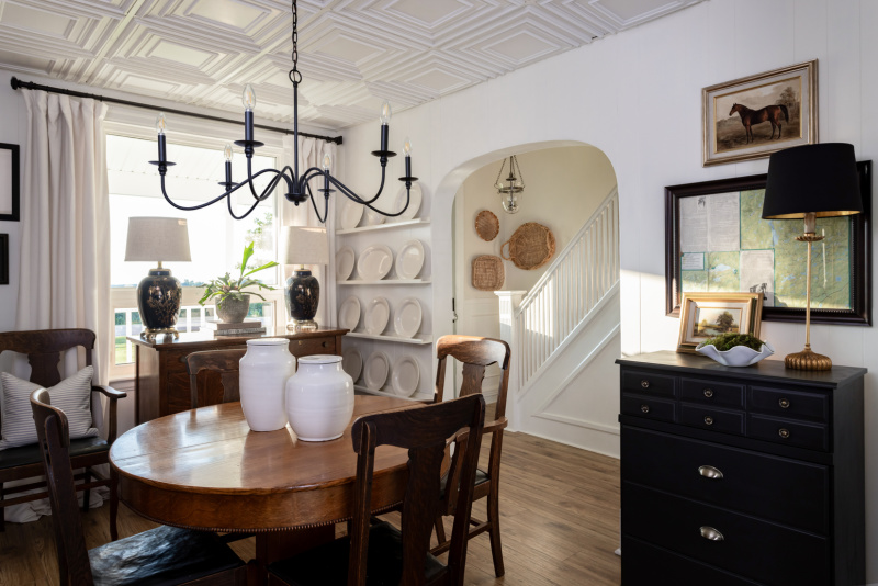 Dining room with antique furniture, black chandelier, white curtains,and equestrian painting.