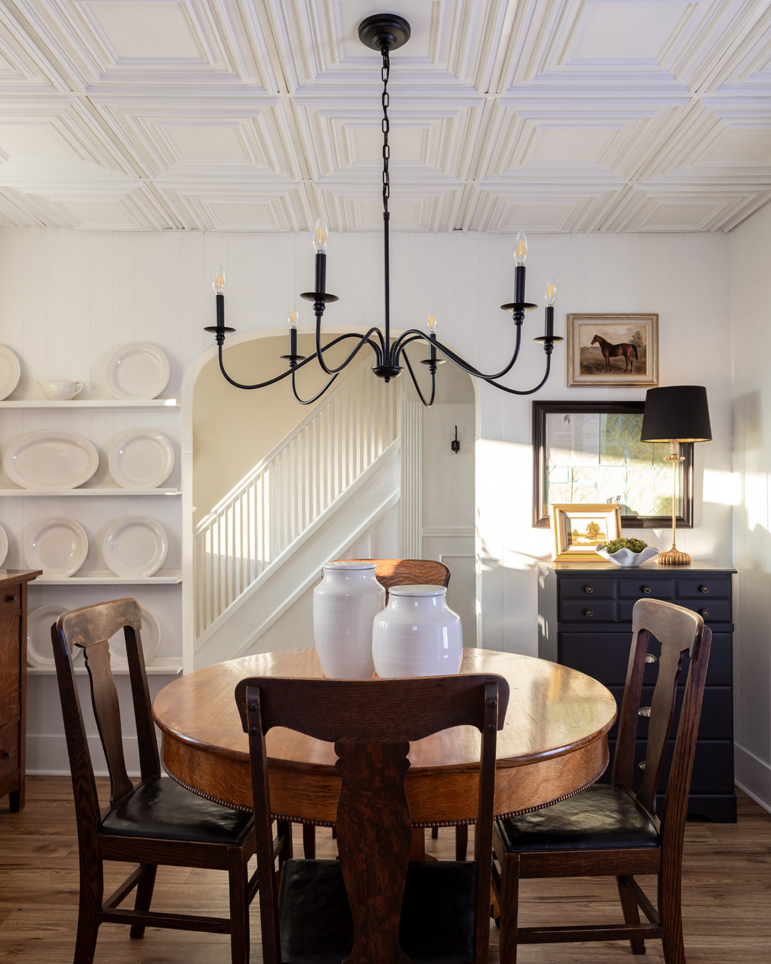 Traditional farmhouse dining room with black ceiling light fixture and plate wall.