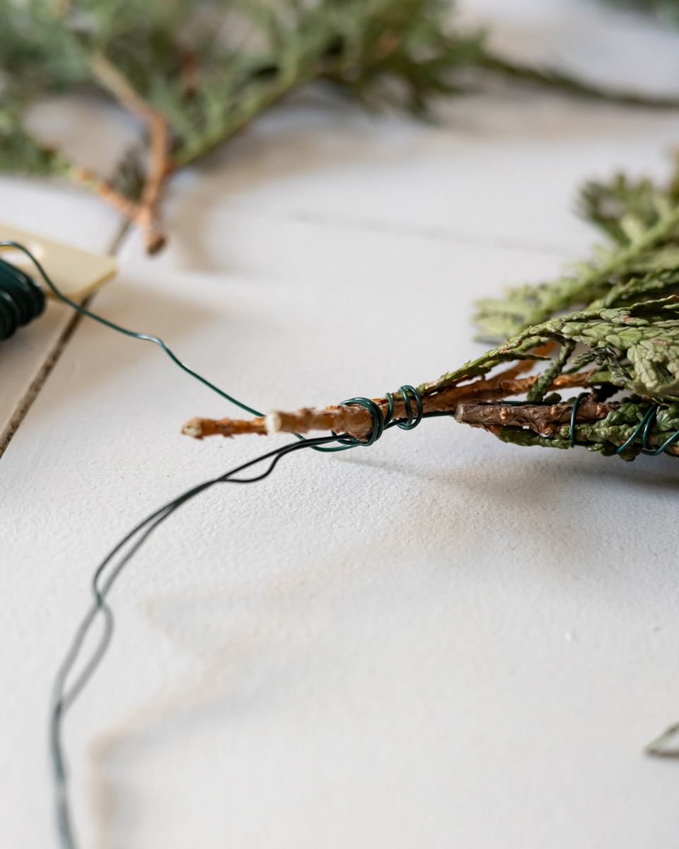 Adding cedar branch pieces to the mini wreath with floral wire.