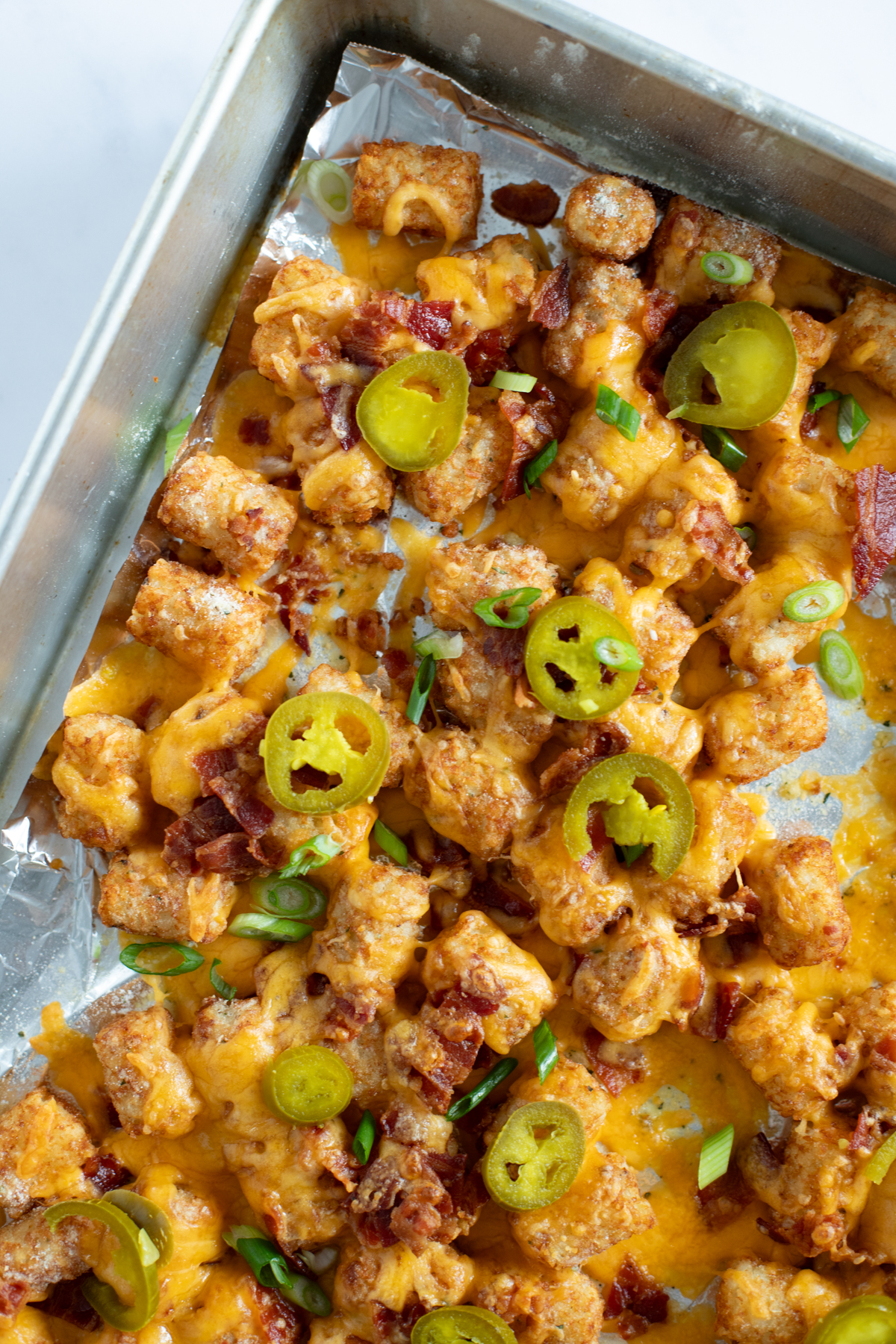 Loaded tater tots on a baking sheet with melted cheese and jalapeños.