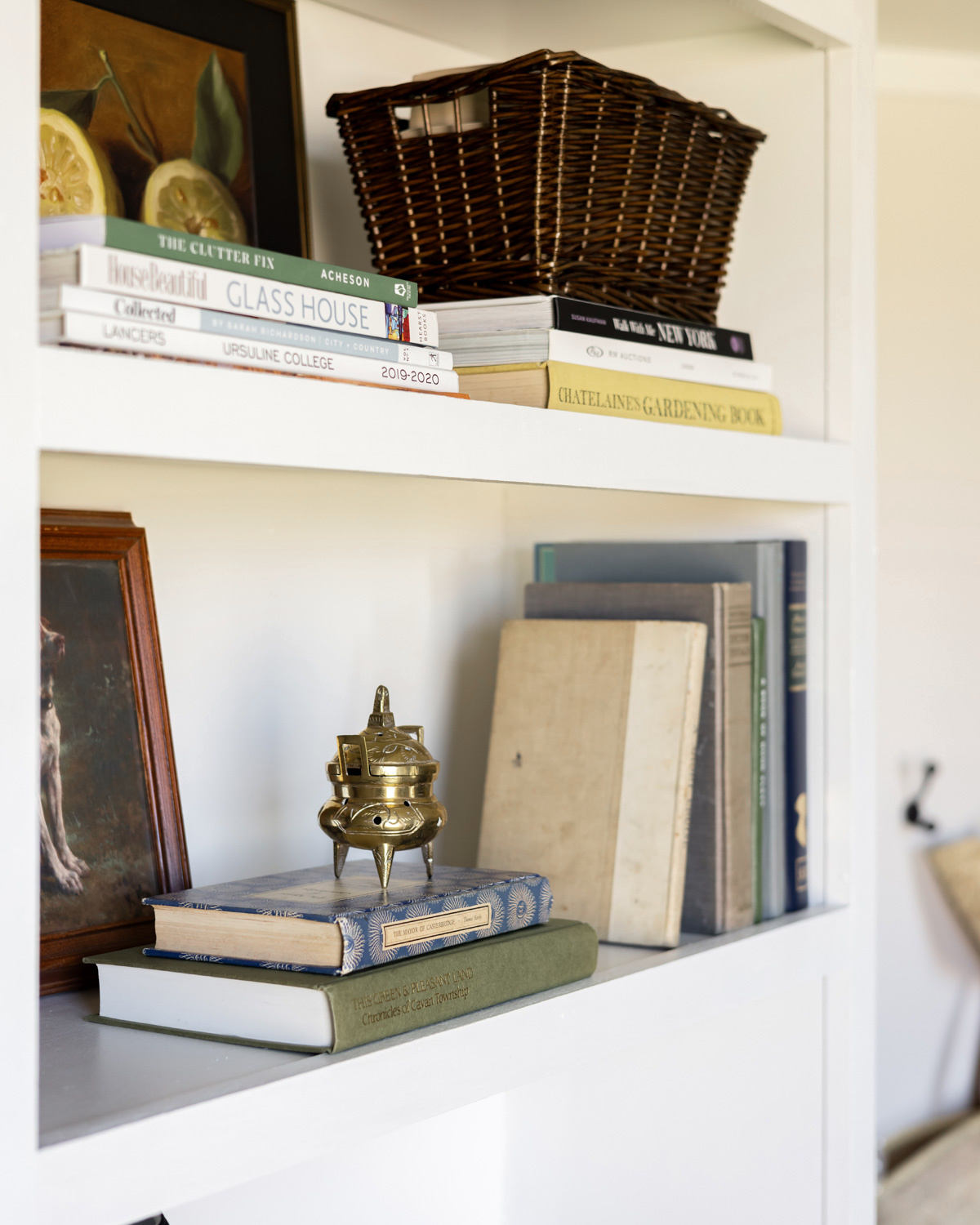 Bookshelf layered with baskets, decorative items, and framed paintings.
