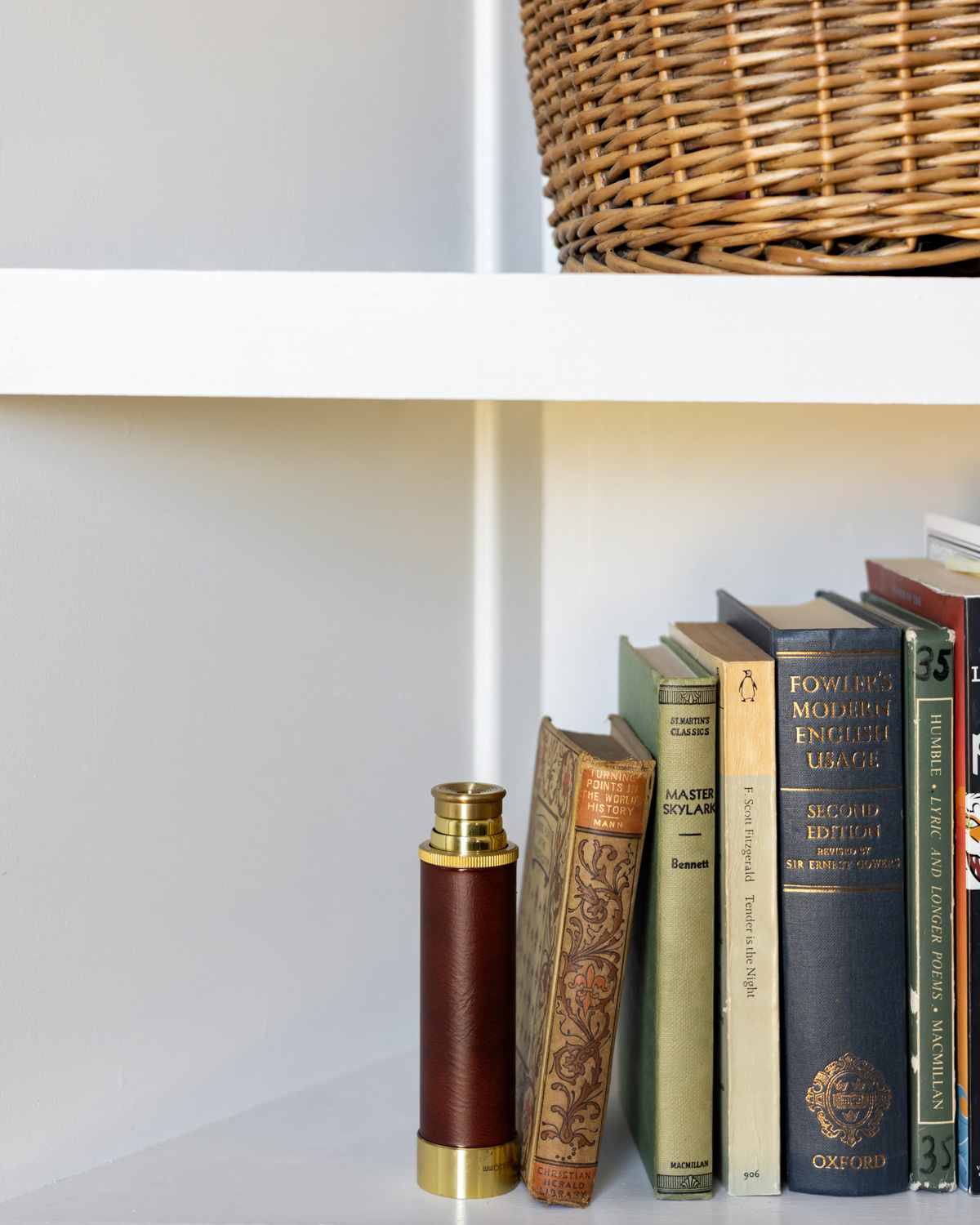 Old books on a shelf with a brass telescope and vintage basket are classic elements of the bookshelf wealth trend.