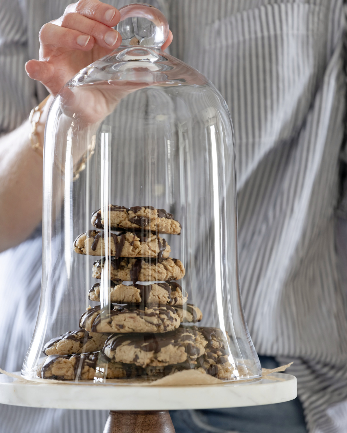A stack of peanut butter chocolate chip cookies under a glass dome.
