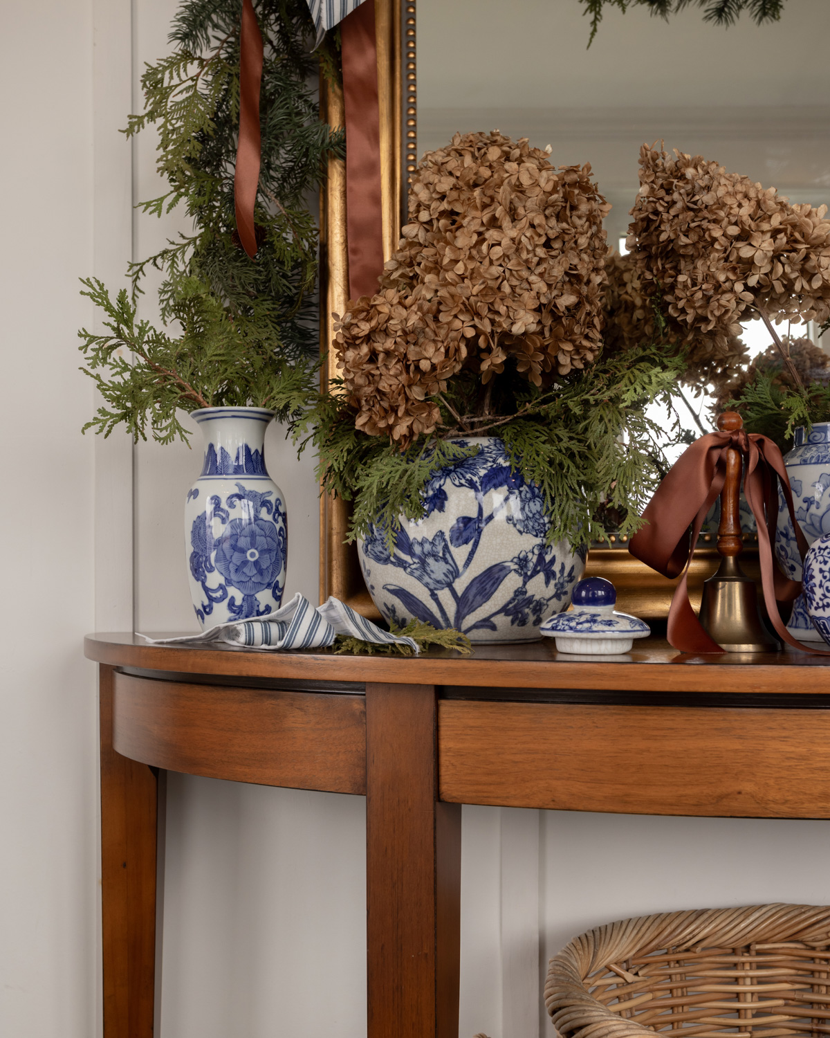A console table decorated with blue and white vases, a gold mirror, and a garland.