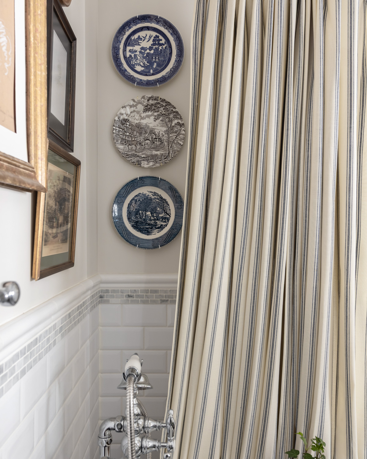 Transferware plates on a bathroom wall wit striped shower curtain.