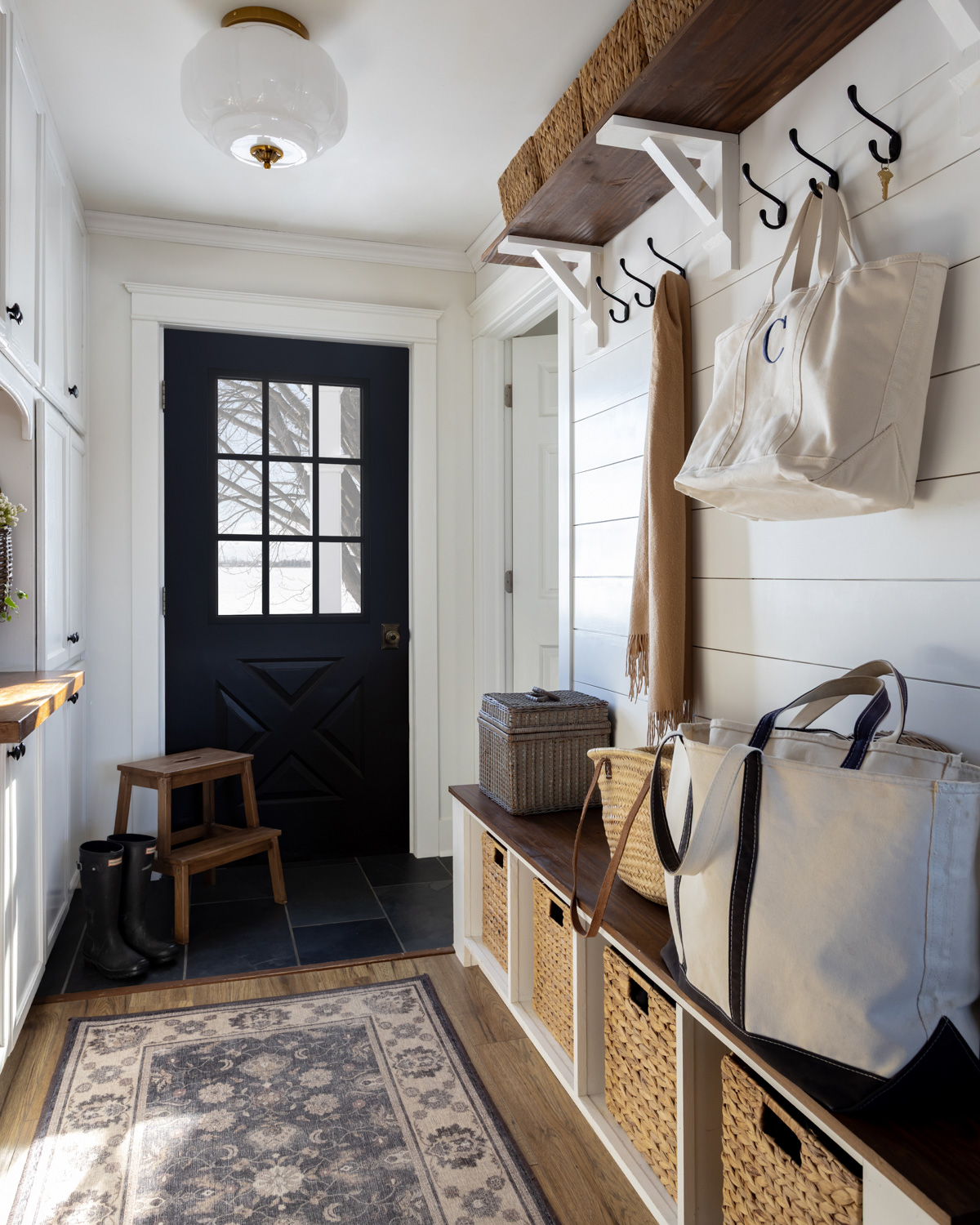 Traditional farmhouse mudroom with white cabinetry and a black door.