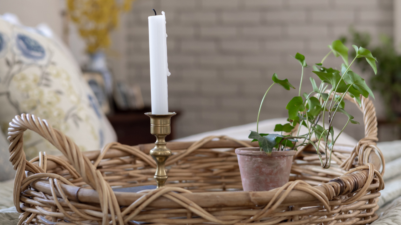 A basket tray on a bed with a small plant and an antique brass candlestick.