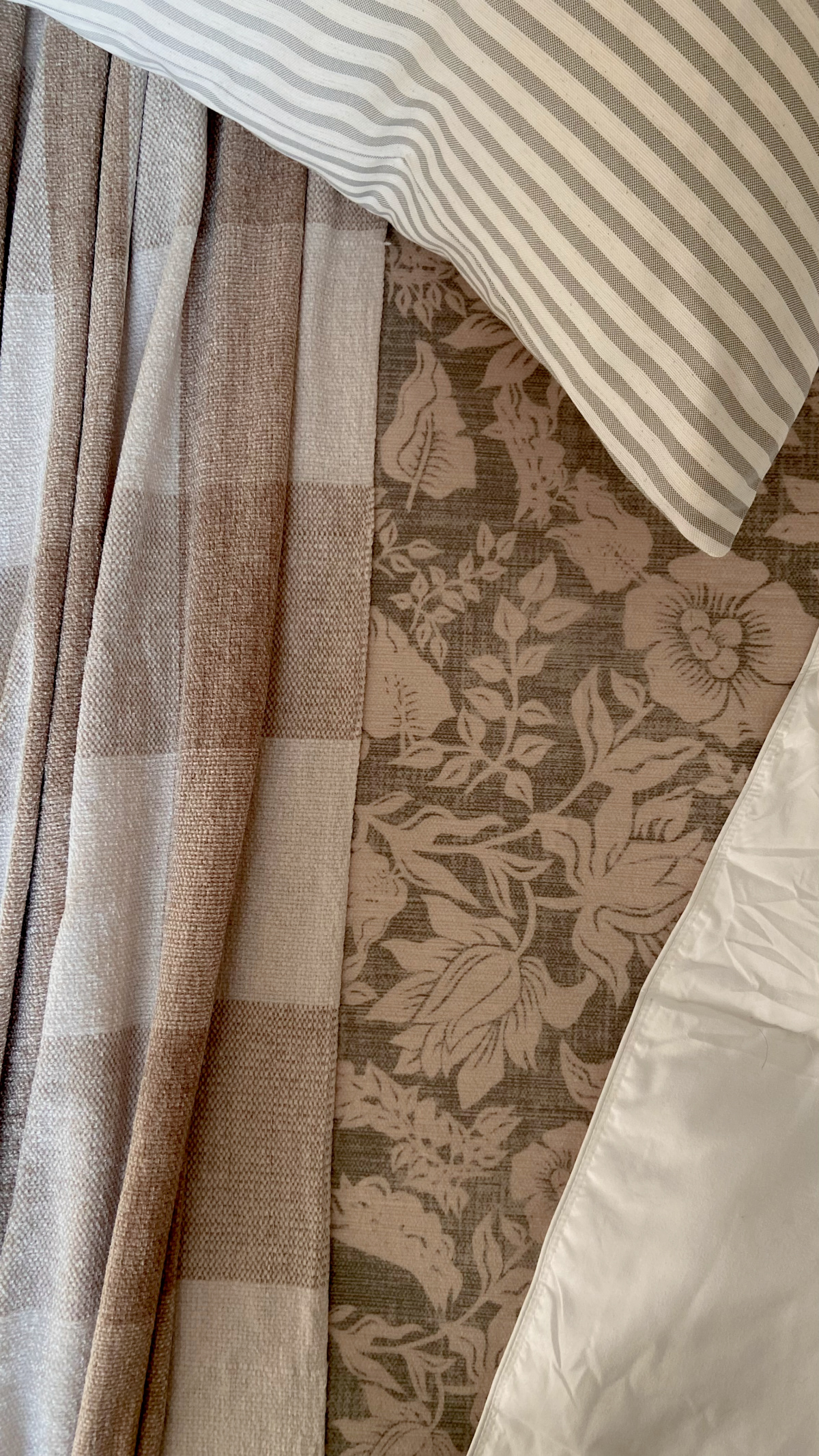 Layers of bedding including a rumpled through blanket, striped cushion, patterned bedspread, and a comforter.