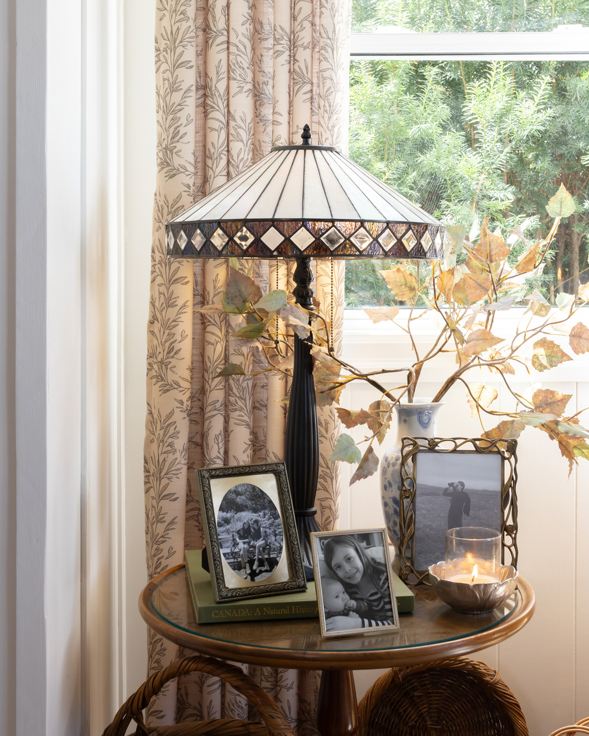 A neutral tiffany style lamp on a small table with family photos and fall leaves.