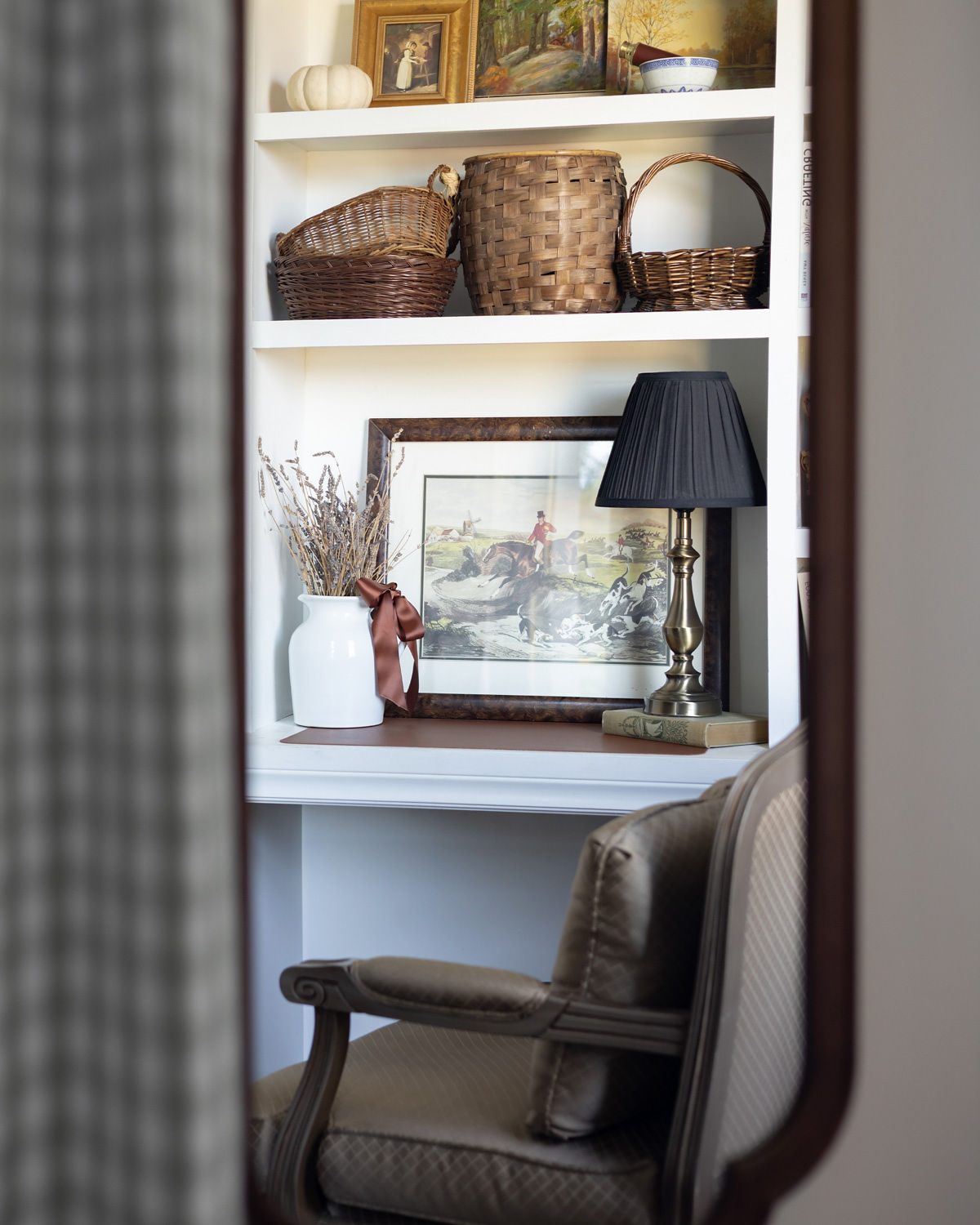 A cozy work area with built-in shelves and desk reflected in a mirror.