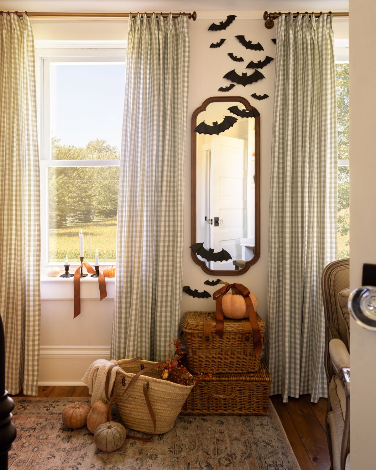 A bedroom with green gingham curtains decorated for Halloween with black paper bats.