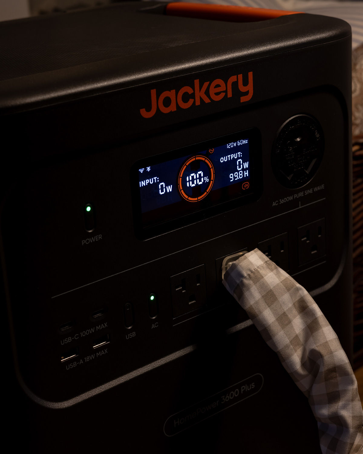 A close up view of the Jackery control panel with a covered cord plugged in.