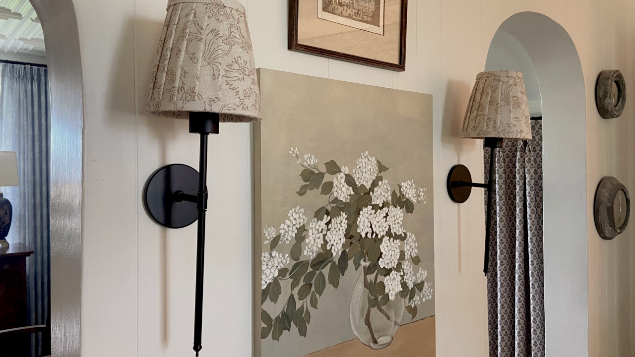 Wall sconces with patterned shades on either side of a painting.